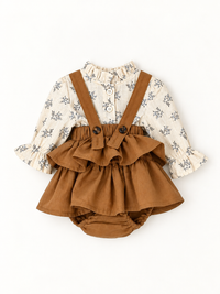 A baby girl's two-piece outfit featuring a cream-colored long-sleeve blouse with a delicate gray floral print and ruffled trim, paired with brown fabric diaper cover overalls that have adjustable shoulder straps and a ruffled waist.