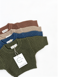 Four ribbed knit baby sweaters in cinnamon, rye, dusty olive, and dusty sapphire, arranged in a flatlay on a white background. 
