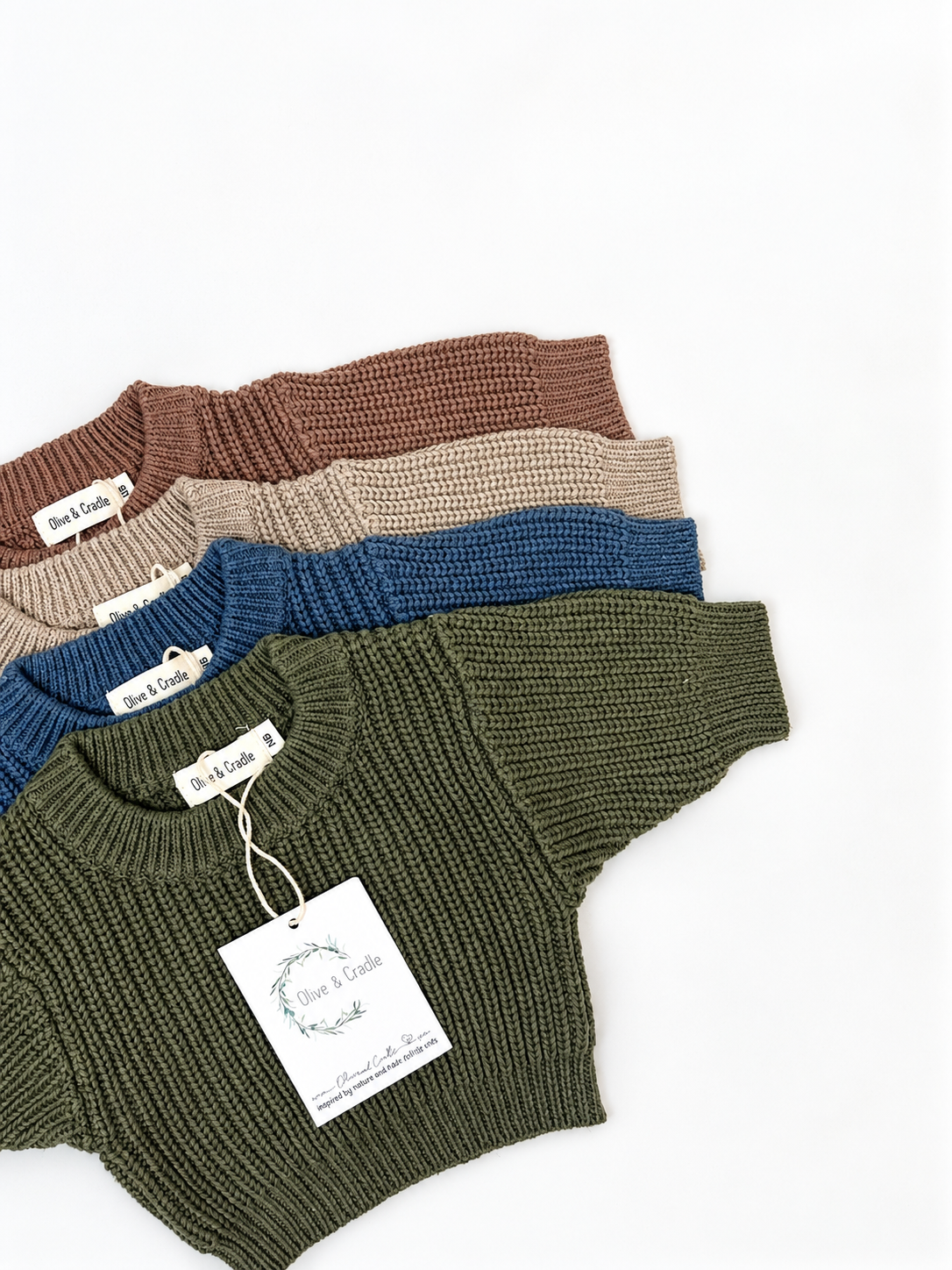 Four ribbed knit baby sweaters in cinnamon, rye, dusty olive, and dusty sapphire, arranged in a flatlay on a white background. 